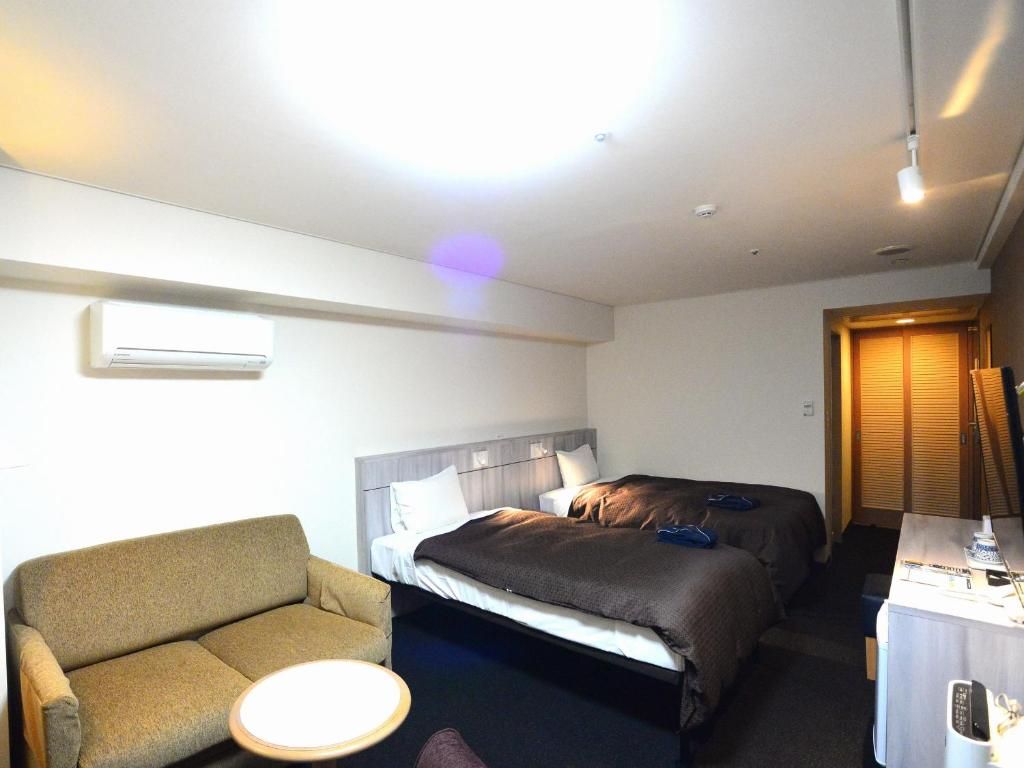 A hotel room with a sofa, two beds, a desk, and an air conditioning unit.