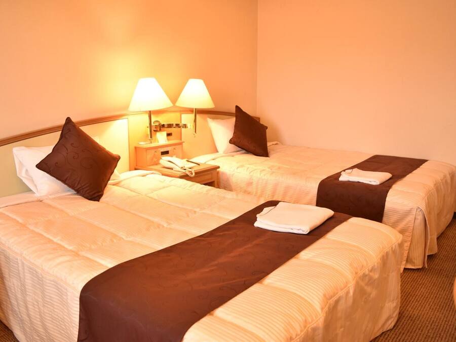 Une chambre d’hôtel avec deux lits, chacun doté d’une tête de lit marron, de draps blancs et d’une petite table de chevet avec une lampe.