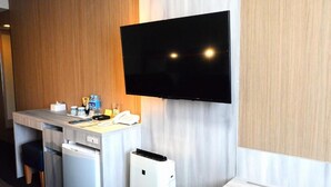 A hotel room with a flat-screen TV mounted on the wall, a small kitchenette with a refrigerator, and a white bedside table. - Sunwest Hotel Sasebo (Sasebo)