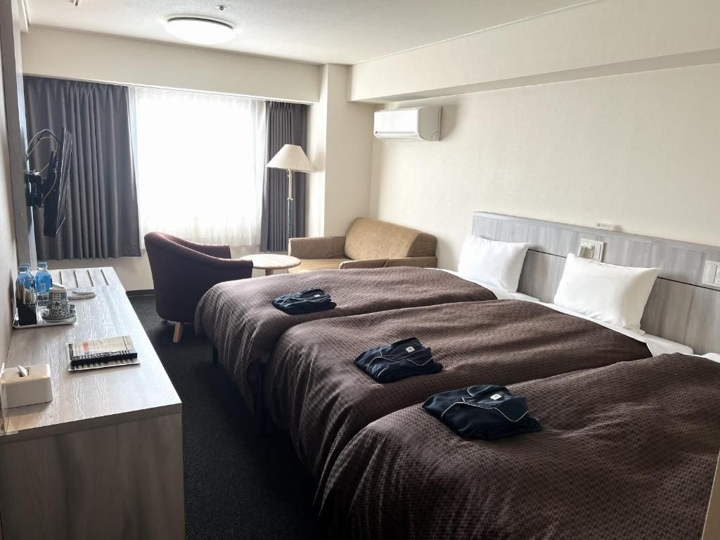 Una habitación de hotel con escritorio, dos camas, una silla y una lámpara.