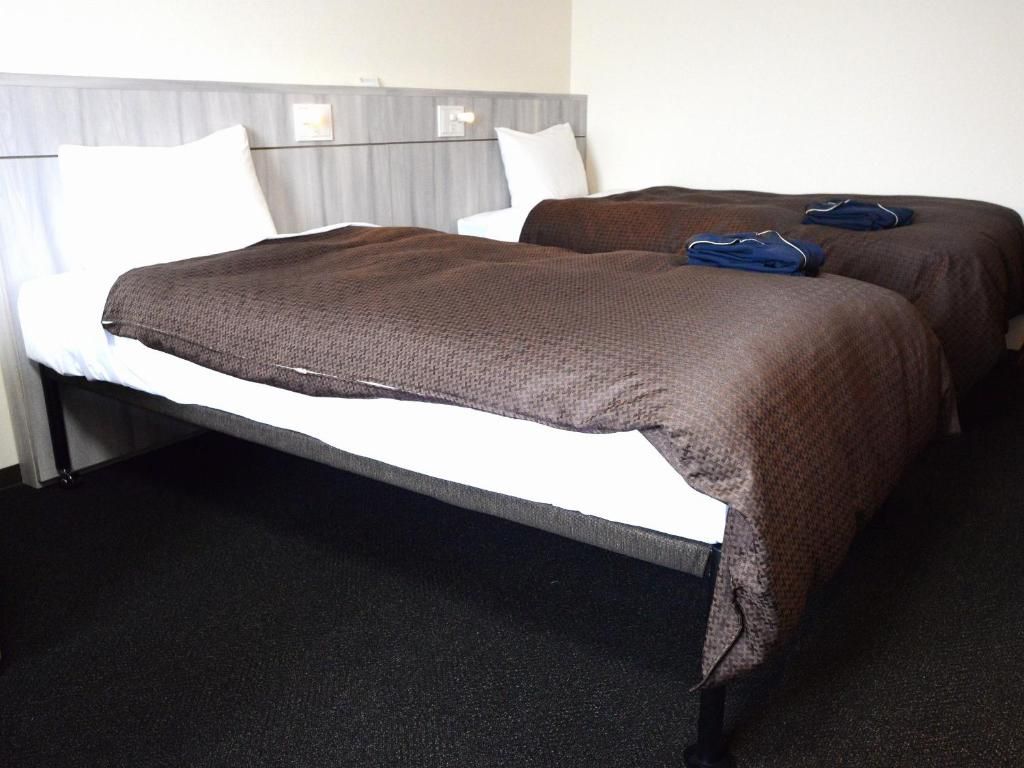 Une chambre d’hôtel avec deux lits, une tête de lit grise et une moquette noire.