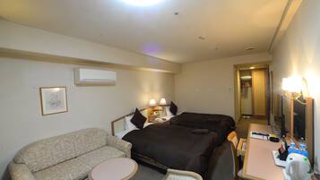 A hotel room with a sofa, two beds, a desk with a lamp, and a mirror.