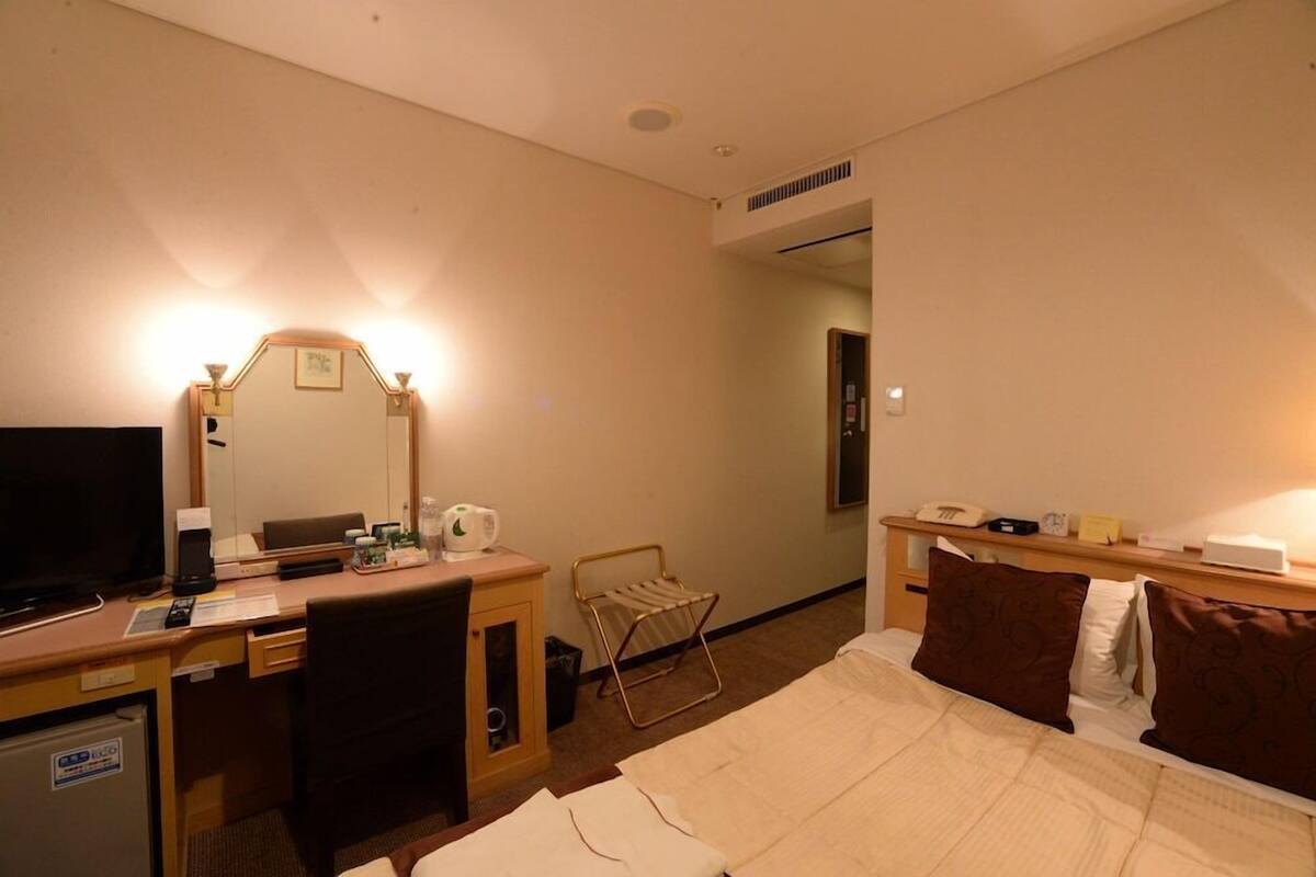 A hotel room with a bed, a desk with a computer, a television, a mirror, and a small radiator.