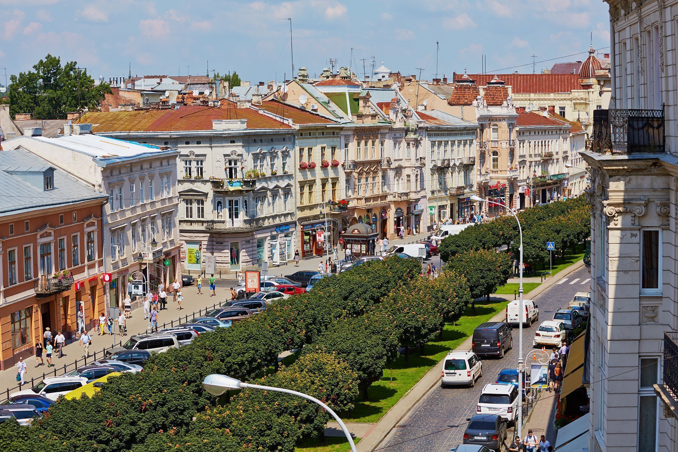 A street lined with historic buildings, a tree-lined median, and parked cars.