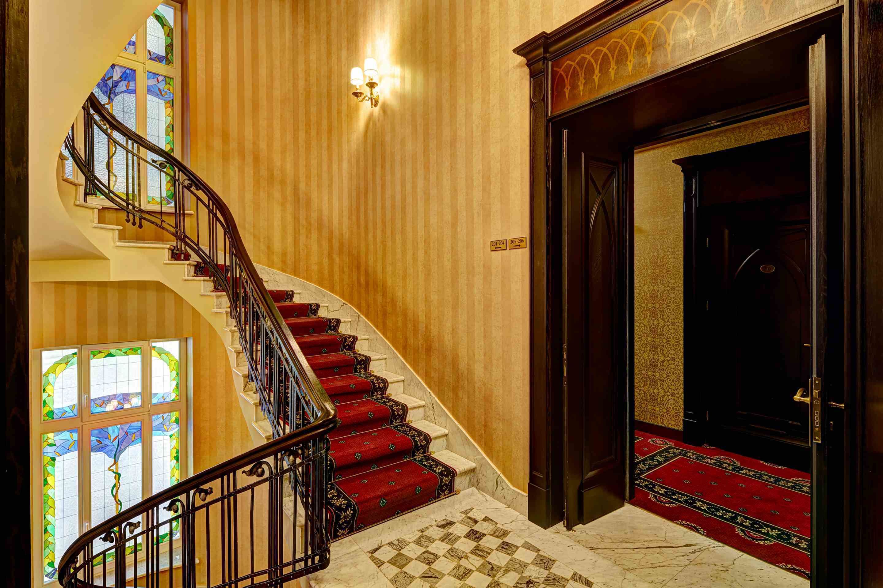 A grand staircase with red carpeted steps, a black metal railing, and a wooden door at the top.