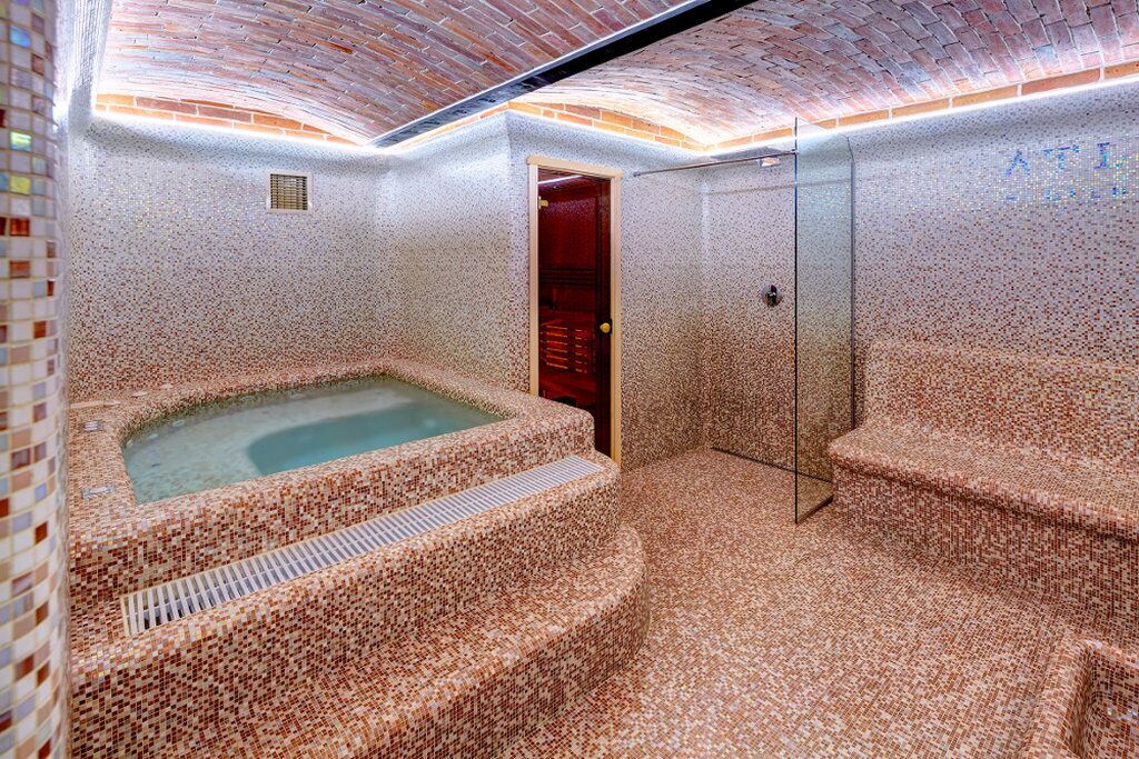Un espace bien-être comprenant un jacuzzi, des marches carrelées et une douche en verre.