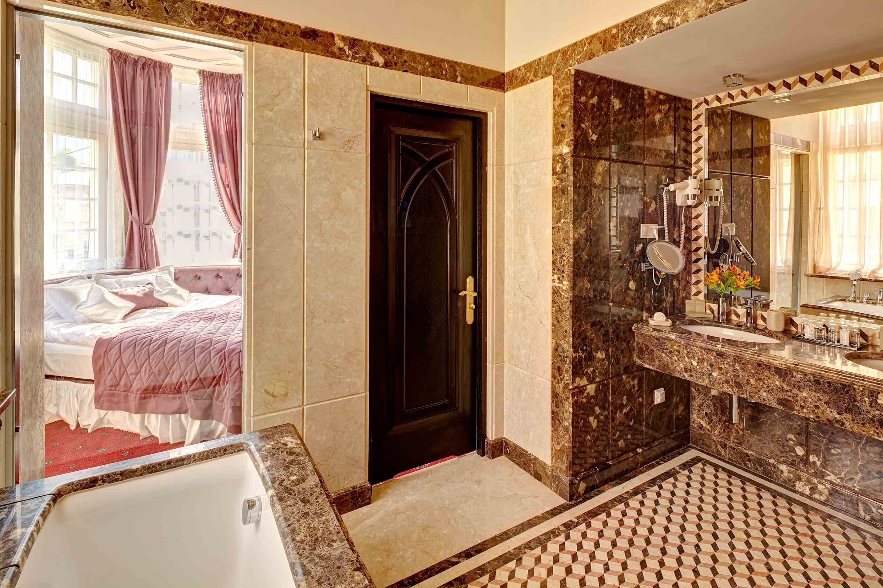 Una habitación de hotel con una cama grande, un baño con tocador de mármol y un piso con estampado de cuadros.