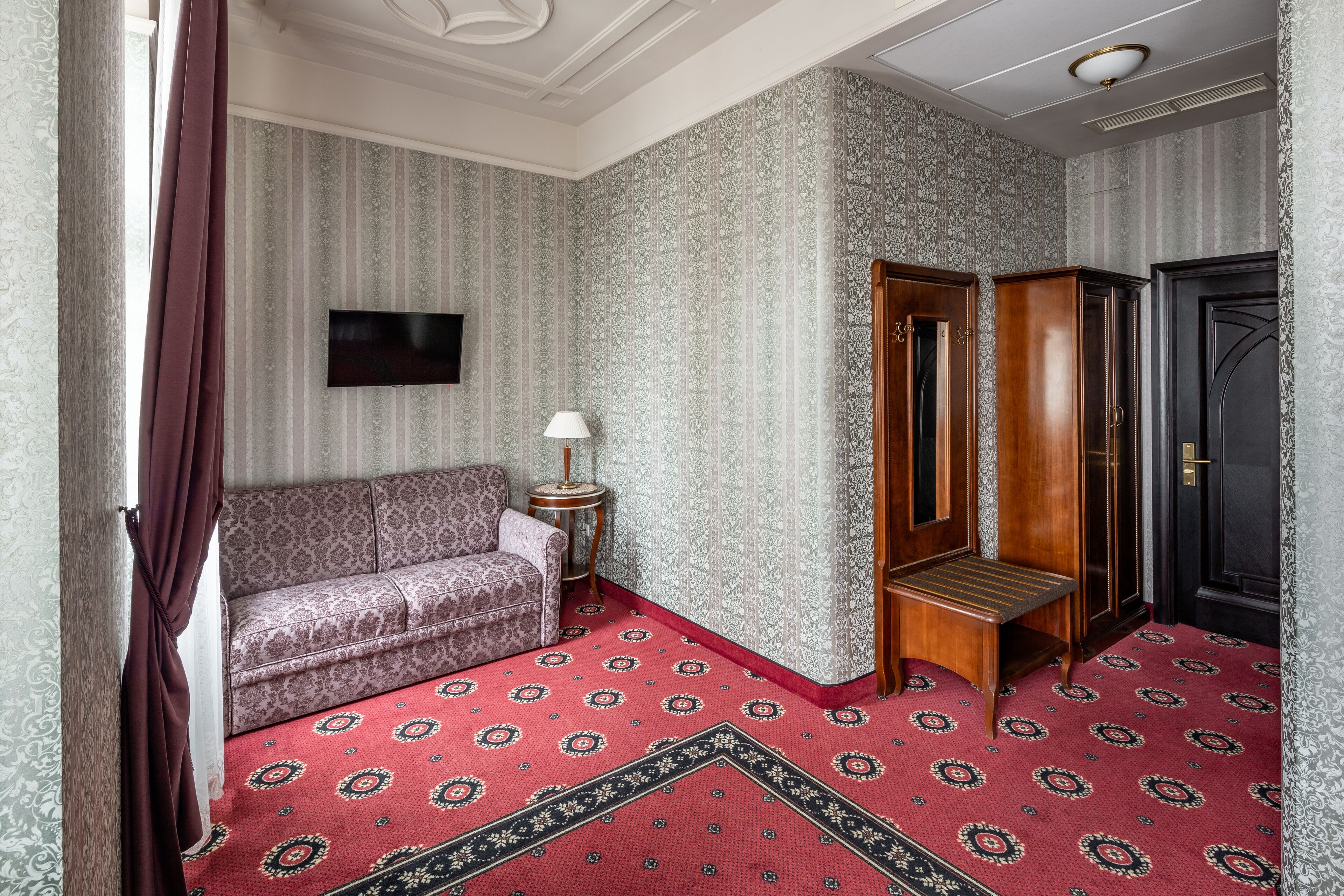 Una habitación con alfombra estampada, un sofá, un banco de madera y una puerta negra.
