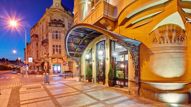 A hotel entrance with a glass canopy, a sign reading "Hotel Atlas," and a cobblestone street.