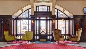 A grand lobby with a red carpet, ornate chairs, and a large arched window.