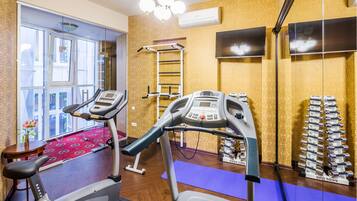 A gym with exercise equipment, a treadmill, a stationary bike, a weight bench, and a wall-mounted TV.