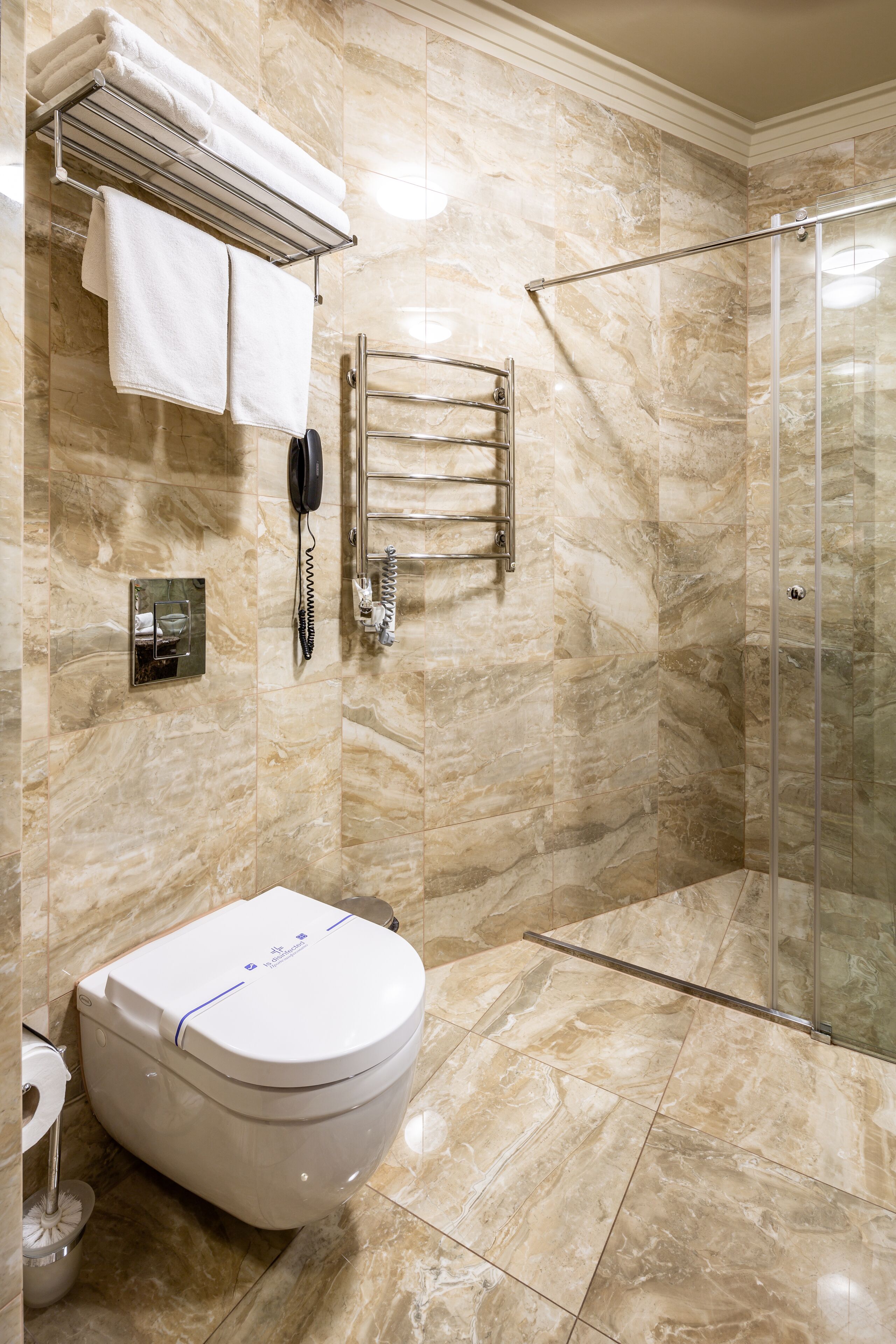 A bathroom with a marble floor, a toilet, a glass shower enclosure, and a towel rack with folded towels.
