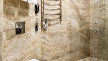 A bathroom with a marble floor, a toilet, a glass shower enclosure, and a towel rack with folded towels.
