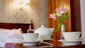A neatly arranged tea set on a wooden table with a vase of pink flowers, in a room with a wooden headboard and wall sconces.