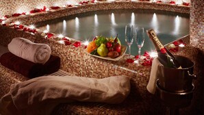 A hot tub with rose petals and candles, a fruit bowl, a bottle of champagne, and towels. - Atlas Deluxe (Lviv)