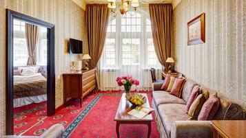 A hotel room with a large bed, a sofa, a coffee table with flowers, a TV, and a large window with curtains.