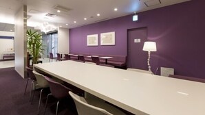 A conference room with a long table, chairs, a potted plant, and a purple wall. - First Cabin Hakata (Fukuoka)