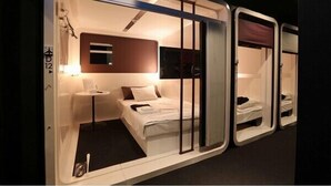 A compact hotel room with a single bed, a small bedside table, a mirror, and a window. - First Cabin Hakata (Fukuoka)
