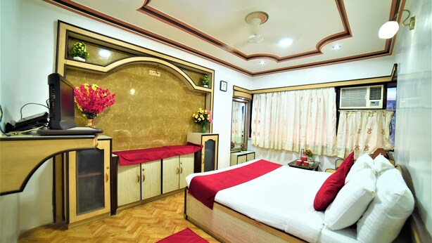 A hotel room with a bed, a desk with a computer, a red rug, and a window with curtains. - Hotel Aircraft International (Mumbai)