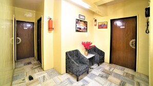 A reception area with two patterned armchairs, a small table with a vase of flowers, and two doors with signs. - Hotel Aircraft International (Mumbai)