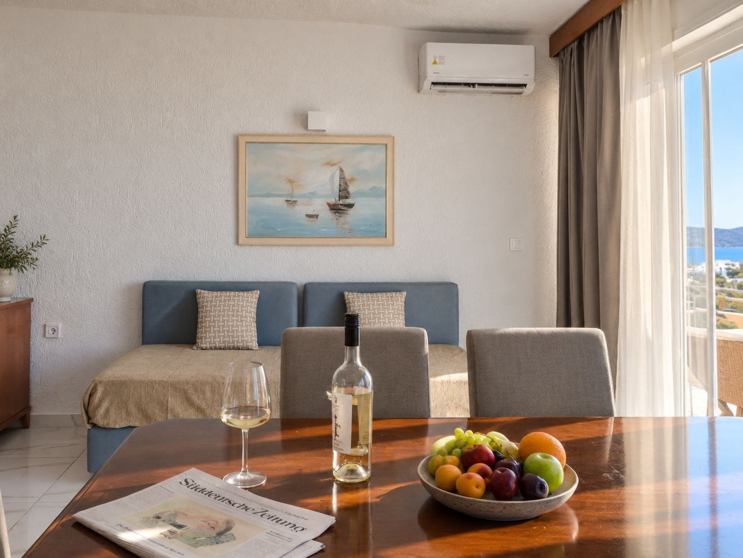 Una stanza con un tavolo da pranzo, un divano, un quadro e vista sul mare.