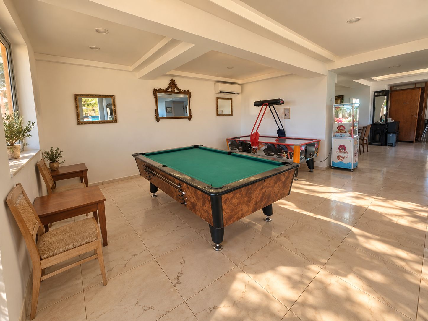 Una mesa de billar en una habitación con zona de comedor, una mesa de billar con cubierta roja y negra, y una máquina de juegos infantiles.