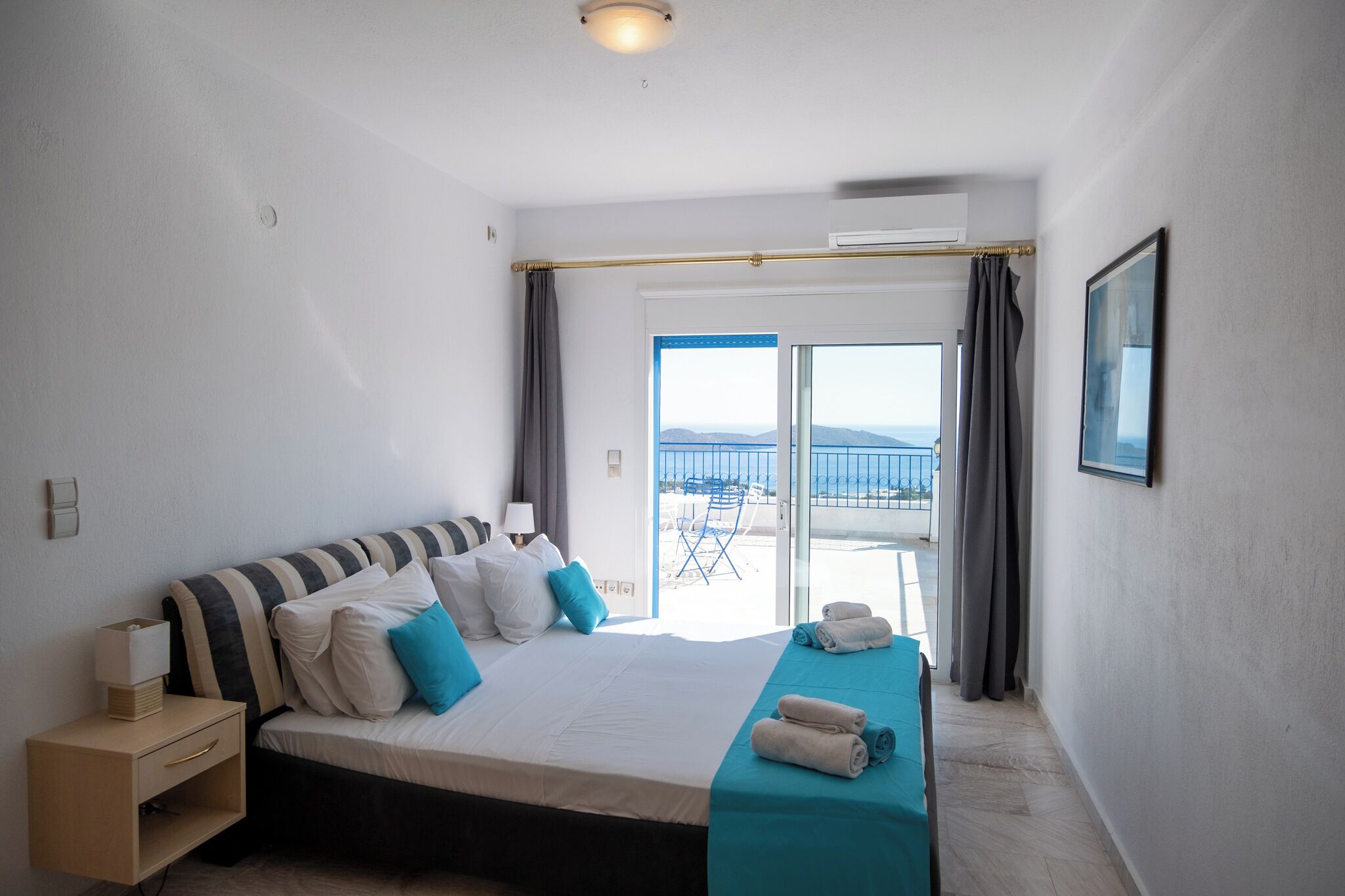 A hotel room with a bed, a nightstand, a window with curtains, and a view of the beach.