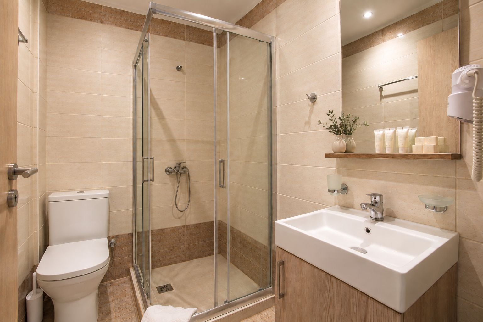 A modern bathroom with a glass-enclosed shower, a white toilet, and a sink with a mirror above.