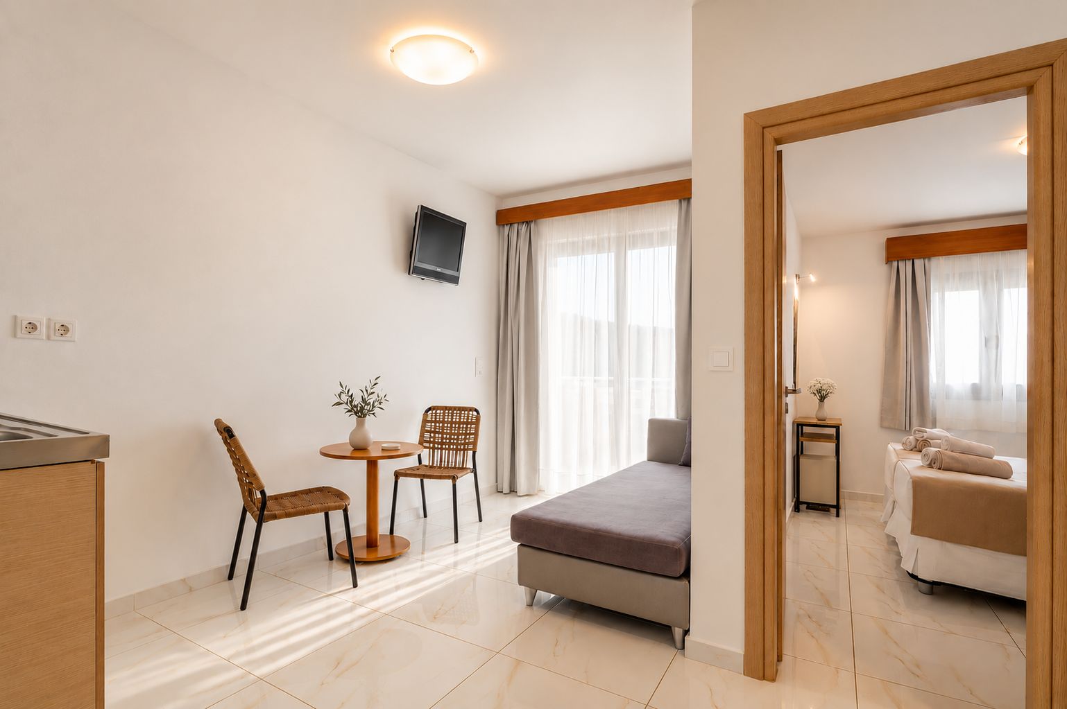 A hotel room with a bed, a small table with chairs, a TV mounted on the wall, and a bathroom visible through an open door.