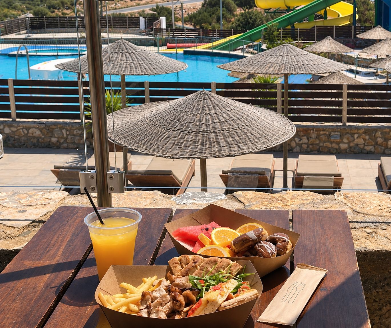 A dining table with food and drinks, outdoor umbrellas, and a pool area in the background.