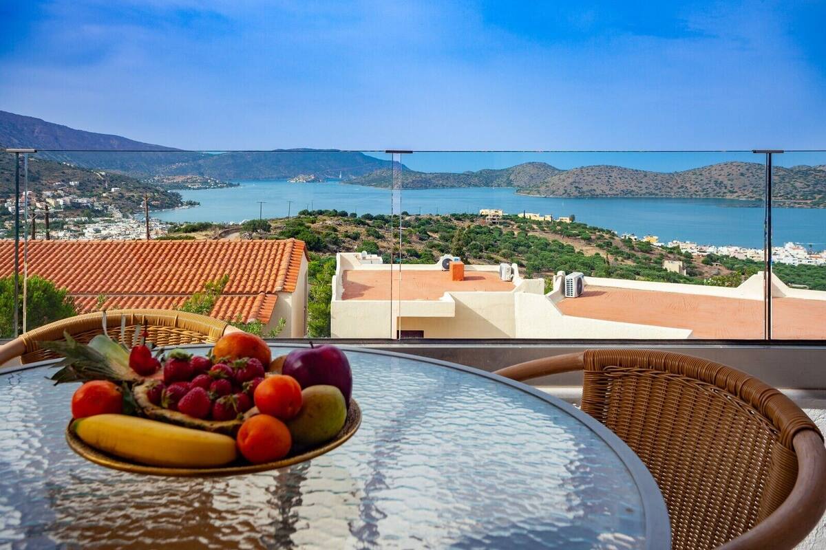 Ein Balkon mit einem Tisch, gedeckt mit Obst, mit Blick auf eine Küstenstadt und das Meer.