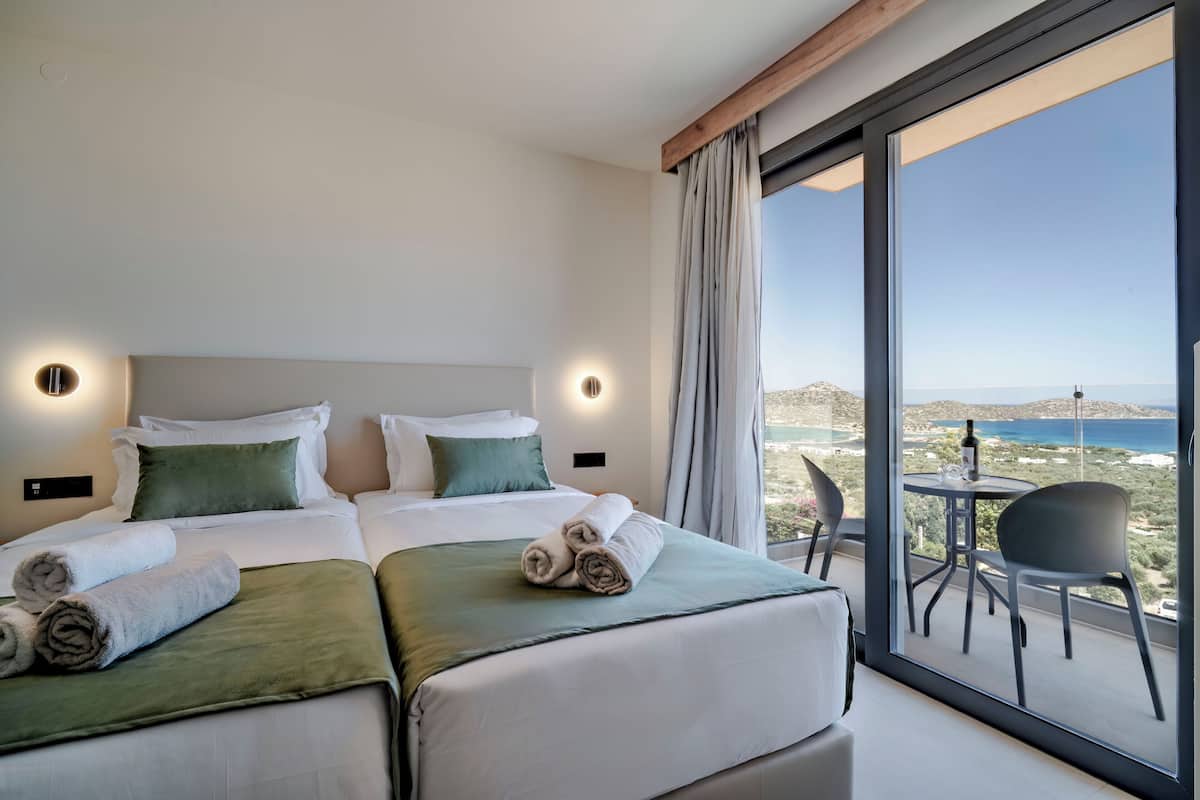 Ein Hotelzimmer mit zwei Betten, einem Balkon mit Tisch und Stühlen und Blick aufs Meer.