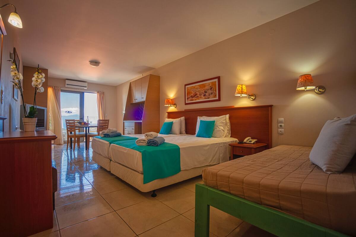 Ein Hotelzimmer mit zwei Betten, einem Schreibtisch, einem Stuhl, einem Tisch und Blick aufs Meer.