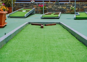 Un petit jeu de billard installé avec un obstacle central, entouré d’un mur de pierre et de plantes en pot.