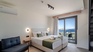 A modern hotel room with a large bed, a sofa, a small table, and a balcony with a view.