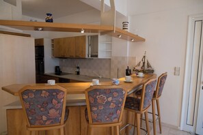 Une cuisine moderne avec des meubles en bois, un îlot central doté de tabourets de bar et un modèle de bateau décoratif.
