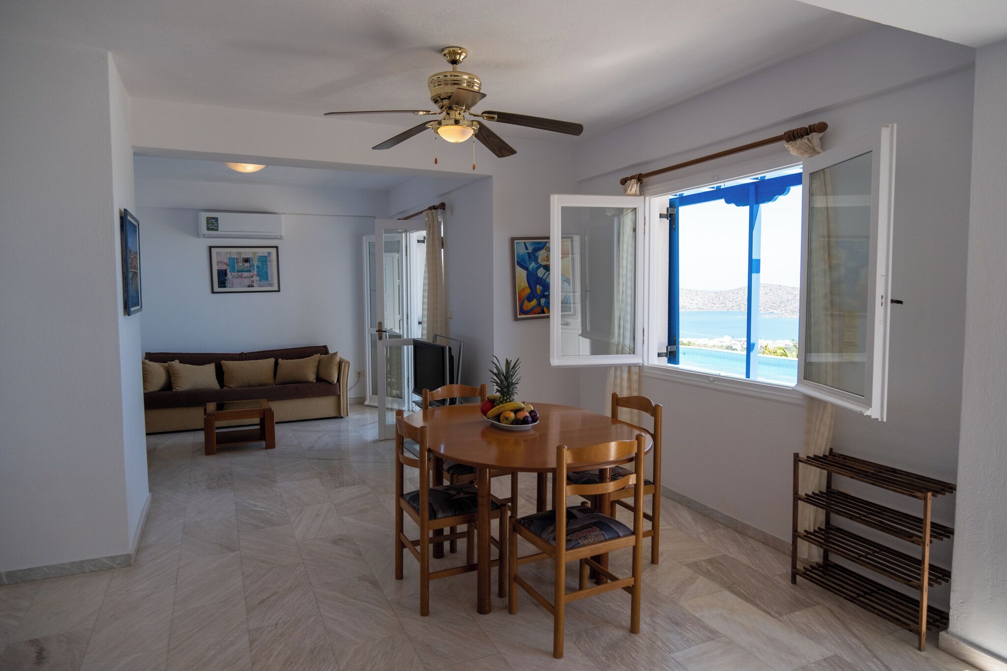 A dining area with a wooden table and chairs, a ceiling fan, and a window with a view of the sea.