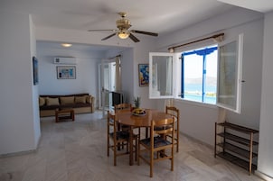 Un comedor con una mesa y sillas de madera, un ventilador de techo y una ventana con vistas al mar.