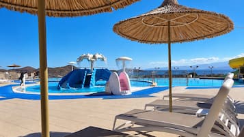 A pool area with lounge chairs, a water slide, and a clear view of the sea.