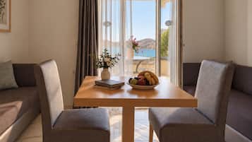 A room with a wooden table, two grey armchairs, a sofa, a vase with flowers, and a bowl of fruit.