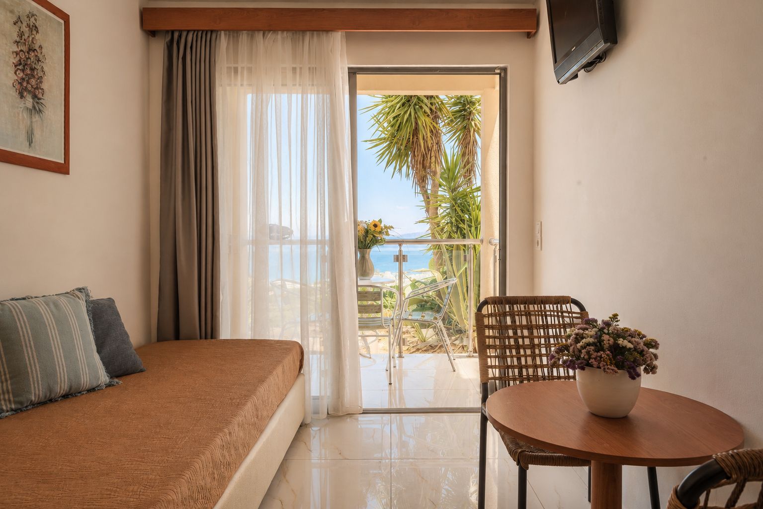 A hotel room with a bed, a chair, a table, and a view of the sea.