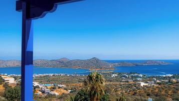 A balcony with a view of a coastal landscape, including a swimming pool and distant hills.