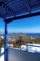 A balcony with a view of a coastal landscape, including a swimming pool and distant hills.