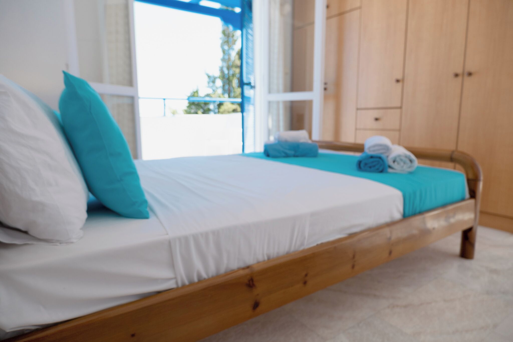 Una cama con ropa de cama blanca y azul, un cabecero de madera y vistas al exterior a través de una ventana.