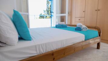 Una cama con ropa de cama blanca y azul, un cabecero de madera y vistas al exterior a través de una ventana.