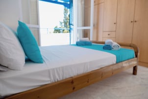A bed with white and blue bedding, a wooden headboard, and a view of the outdoors through a window.