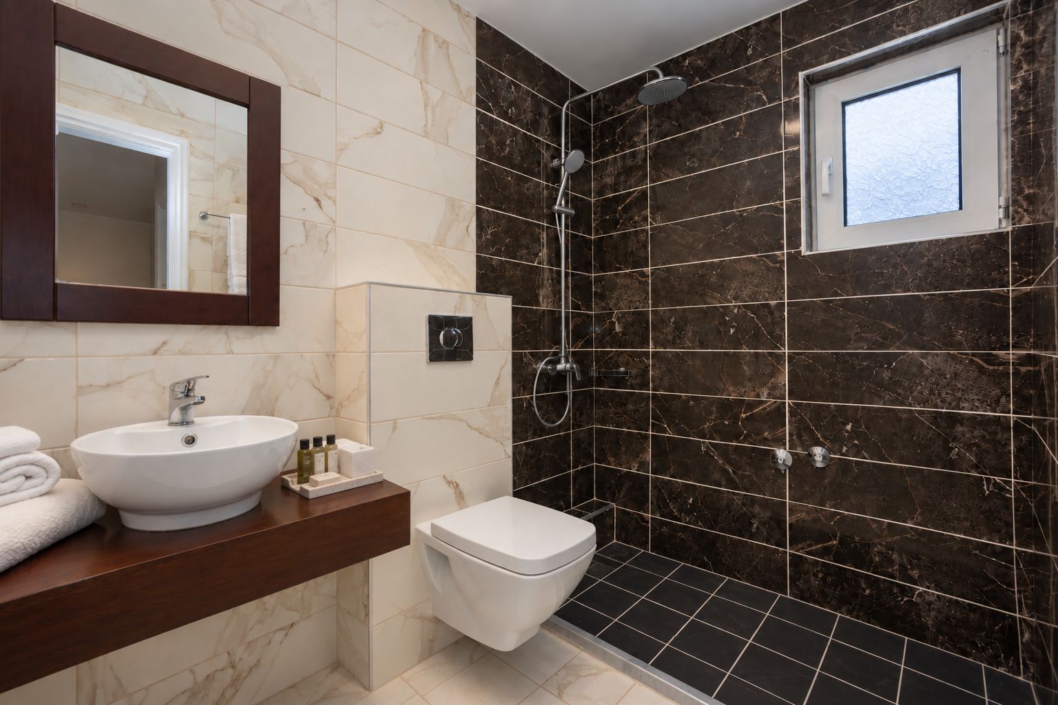 Un bany amb un tocador de marbre, un lavabo, un vàter i una dutxa amb porta de vidre.