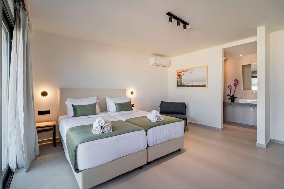 Ein modernes Hotelzimmer mit einem großen Bett, Nachttischen, einem Schreibtisch und einem durch eine offene Tür einsehbaren Badezimmer.