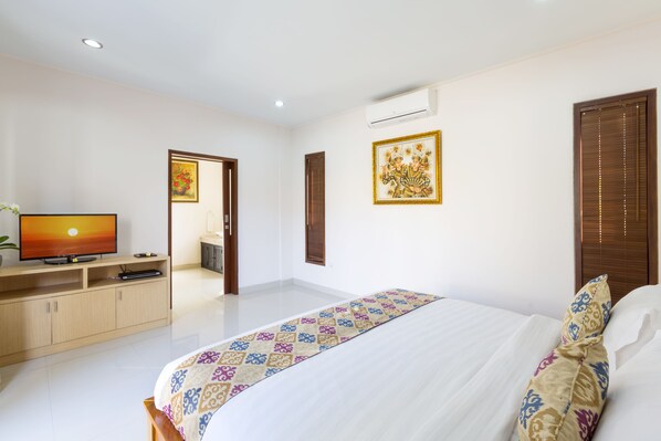 A bedroom with a bed, a TV, a cabinet, and a door leading to another room. - Kubal Villa and Living Seminyak (Seminyak)