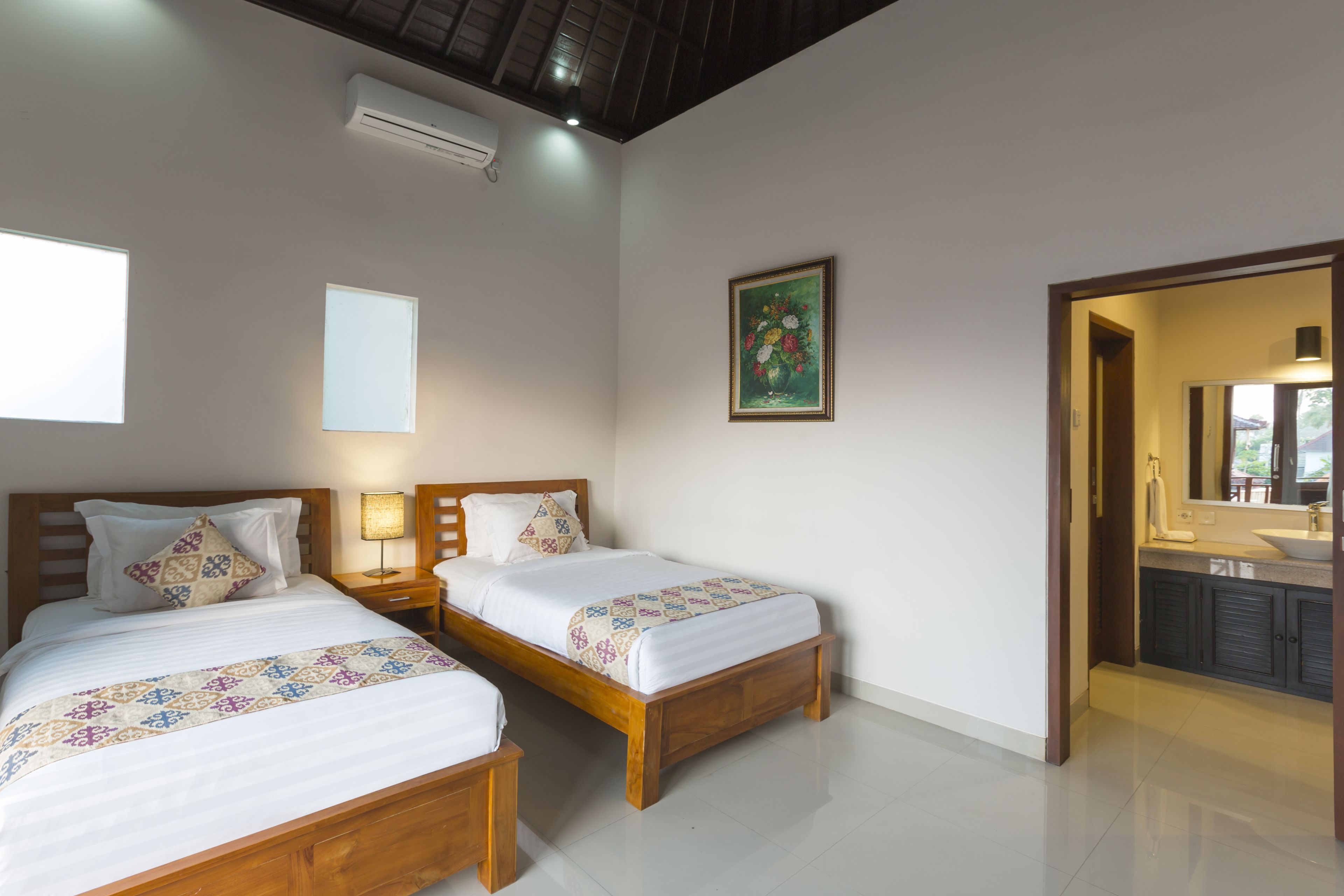 A bedroom with two beds, a bedside table, a wall-mounted air conditioner, and a painting.